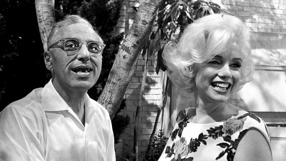 Eine Mann und eine blonde Frau lächeln.