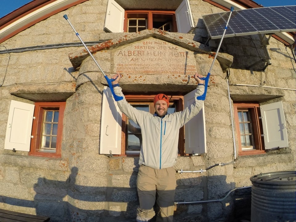 Chrigel Maurer vor einer SAC-Hütte hält seine Krücken in die Luft.
