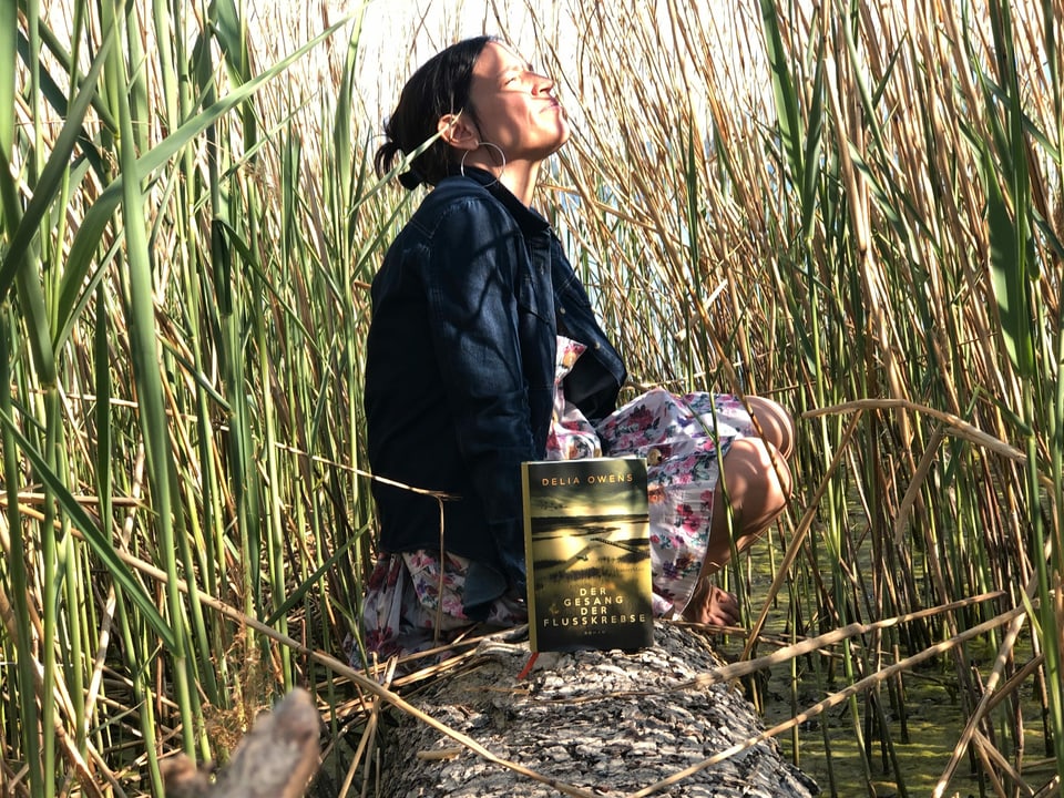 The Power of Nature Annette König sitzt im Schilf. Vor ihr auf einem Baumstamm steht der Roman «Der Geang der Flusskrebse» von Delia Owens