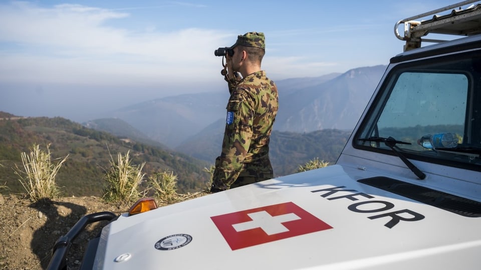 Ein Schweizer Soldat vor einem Jeep mit Schweizerflagge in den kosovarischen Bergen.