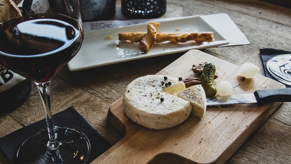 Weichkäse und ein Glas Rotwein. Im Hintergrund Apéro-Blätterteigstangen.