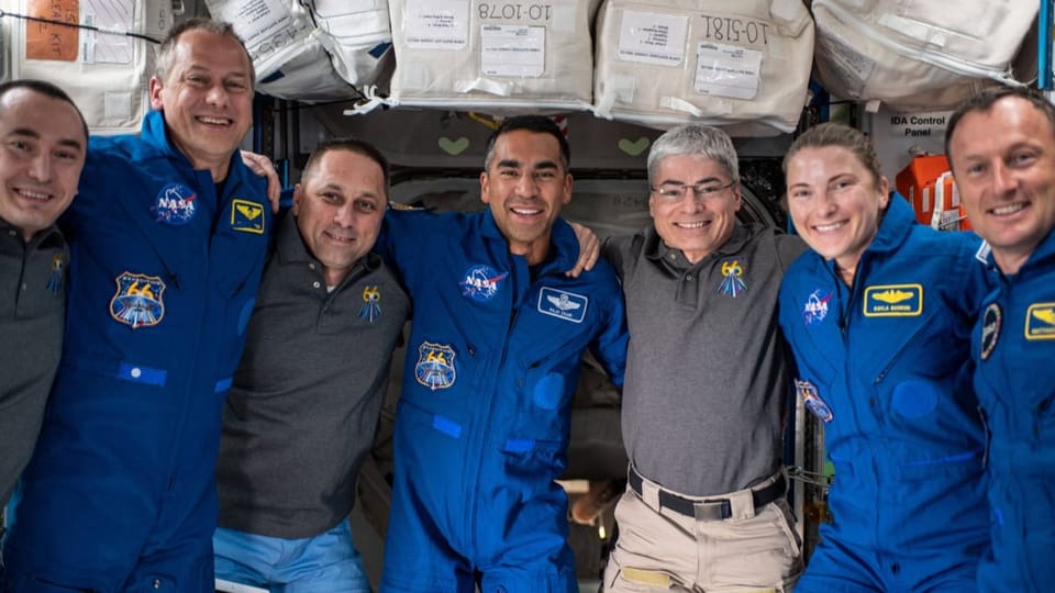 Sechs Astronauten und eine Astronautin umarmen sich für ein Foto.