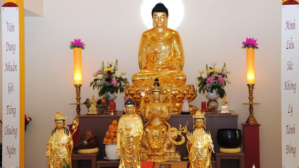 In einem Raum stehen eine grosse und vier kleinere goldene Buddha-Statuen