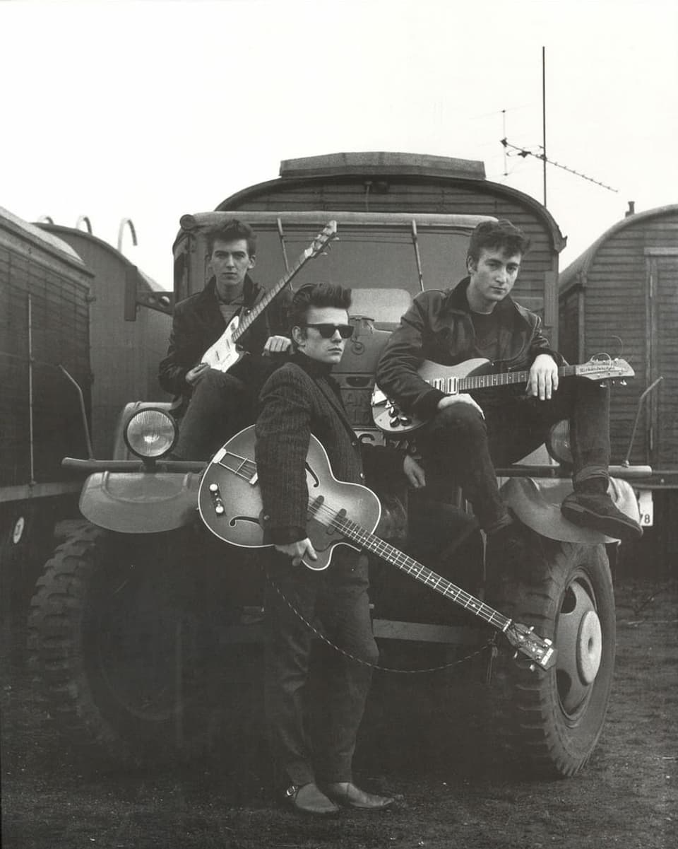 Drei junge Männer in Lederjacken posieren mit Gitarren.
