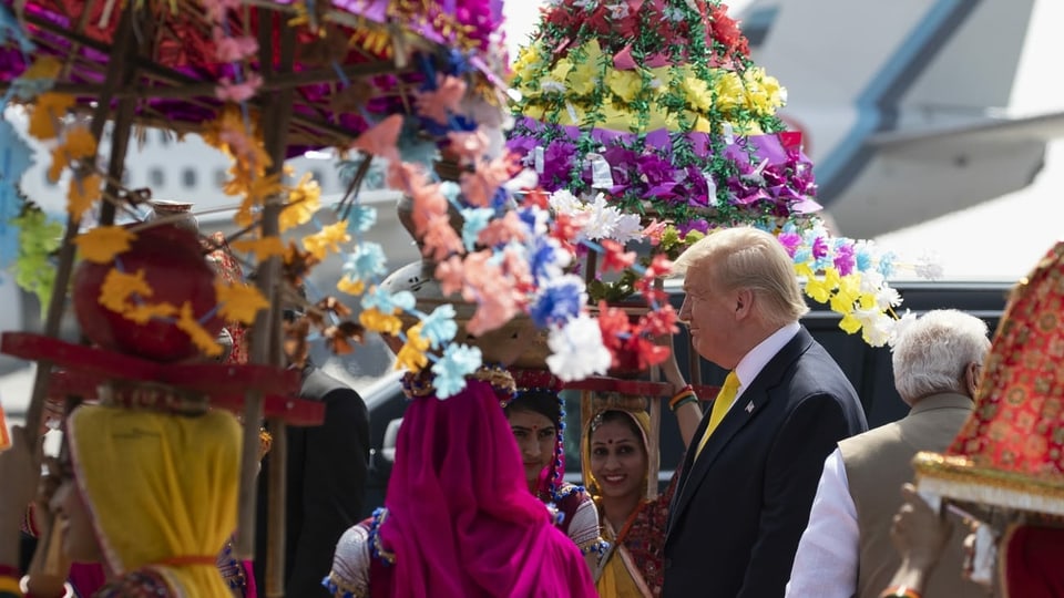 Trump geht durch ein Spalier von in farbige Saris gekleidete Inderinnen