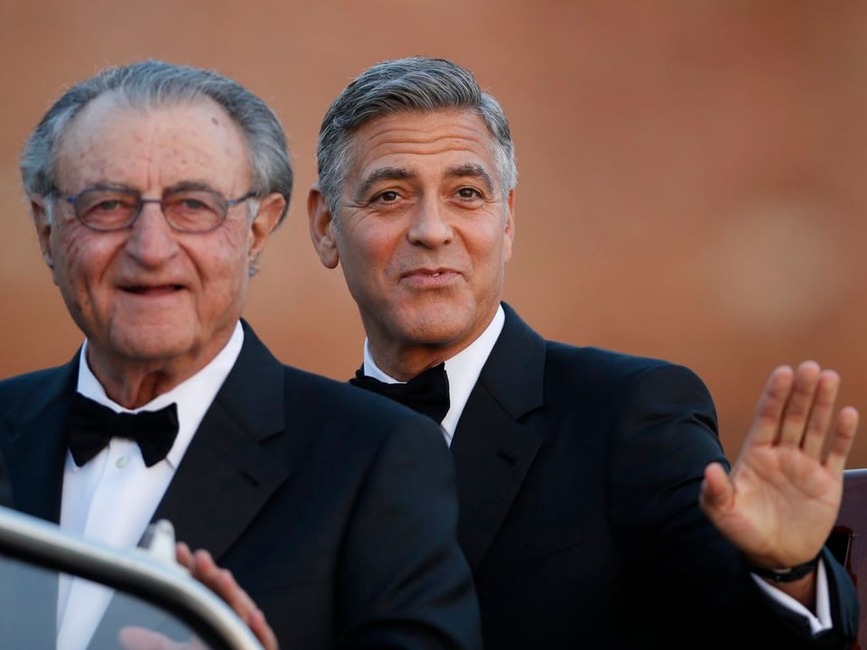 Der Schauspieler George Clooney trägt Smoking und winkt in die Kamera.
