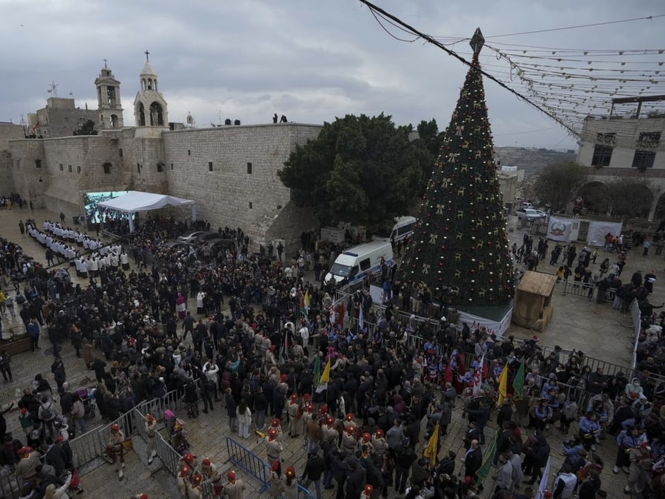 Auf dem Krippenplatz vor der Geburtskirche von Bethlehem steht ein Christbaum. Viele Menschen drängen sich davor.