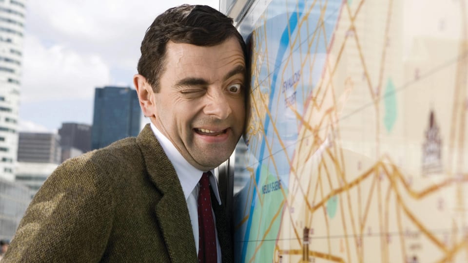 Auf dem Bild ist Mr. Bean zu sehen, wie er listig eine Karte von der Seite beäugt.