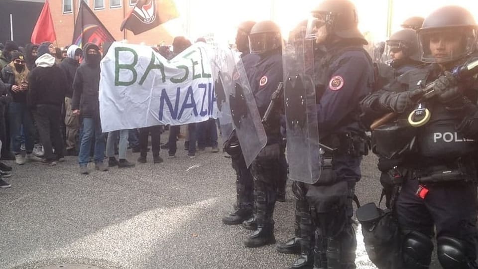 Links sieht man Demonstrant:innen, rechts Politisten in Kampfmontur.