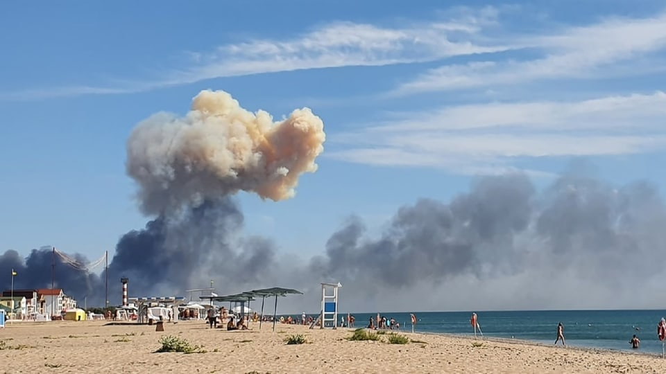 Menschen am Strand, am Horizont steigen Rauchwolken auf