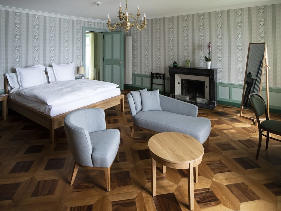 Blick in ein Schlafzimmer im Schloss Schadau: Ein Bett, moderne Sessel, Holzboden. 
