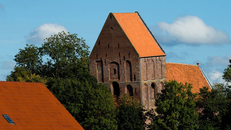 Eine Kriche hinter einem Waldstück, der Turm steht schief.