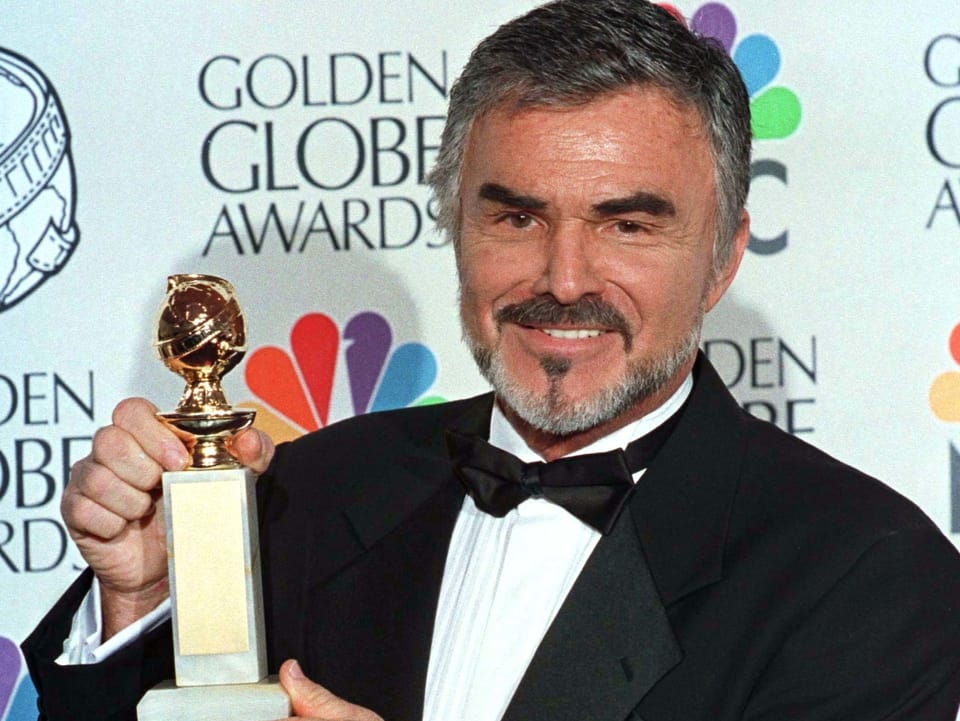 Burt Reynolds posiert vor einer Fotowand mit dem Golden Globe.