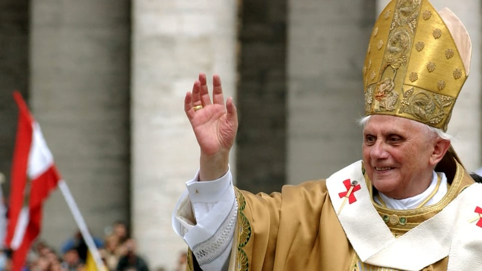 Der Papst hebt die Hand für einen Segen und schaut in die Menschenmasse.