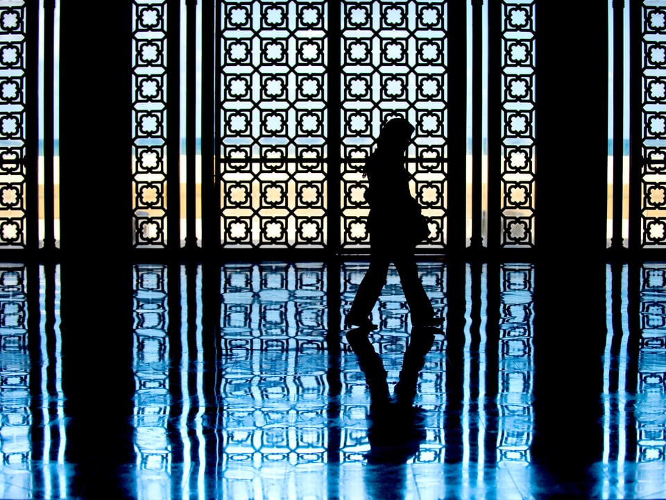 Eine Frau läuft durch eine Moschee, man sieht nur ihre Silhouette.