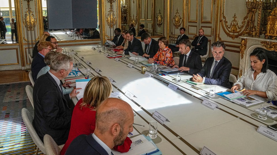 Emmanuel Macron und die Ministerinnen und Minister seiner Regierung sitzen an einem grossen Tisch.