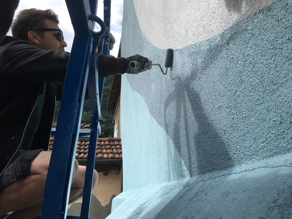 Künstler bringt mit Roller Farbe auf die Fassade.