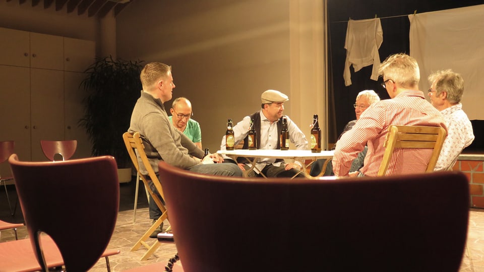 Männer sitzen um einen Tisch und diskutieren bei Bier.