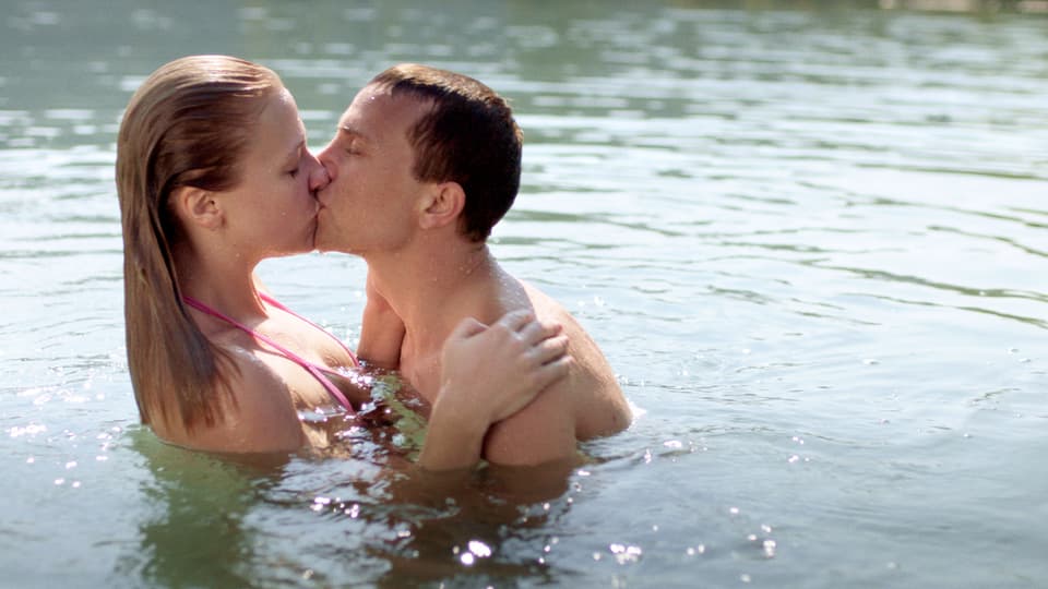 Ein junges Paar schwimmt im See und küsst sich.