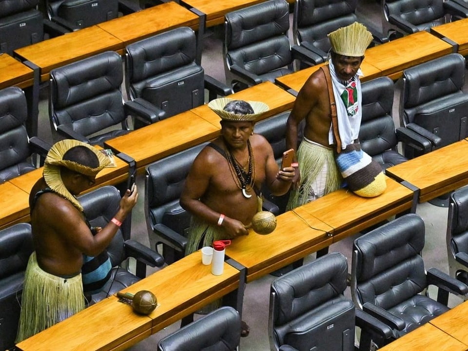 Indigene Männer in traditioneller Kleidung sitzen an einem Sitzungstisch.