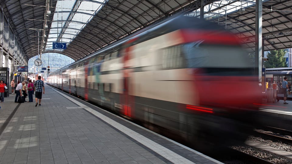 Ein Zug braust durch den Bahnhof Olten, daneben Perron mit Menschen.