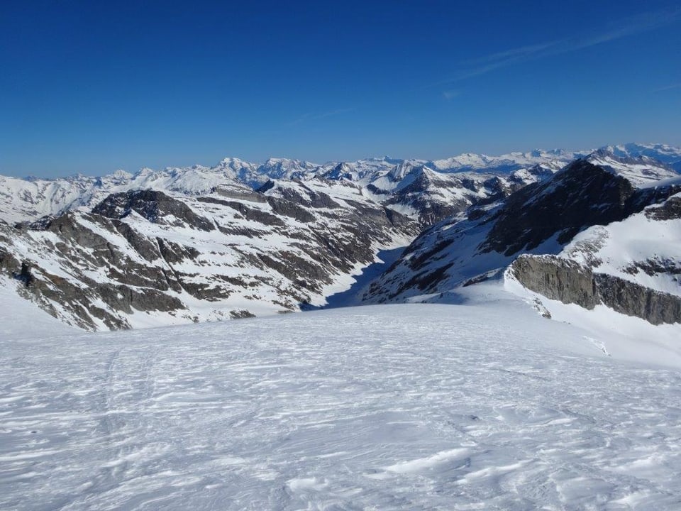 Blauer Himmel, verschneite Alpen, Blick auf ein langgezogenes Tal. 