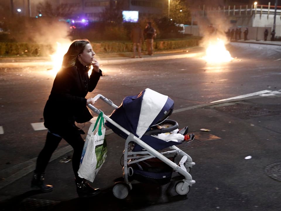 Frau mit Kinderwagen vor brennenden Barrikaden.