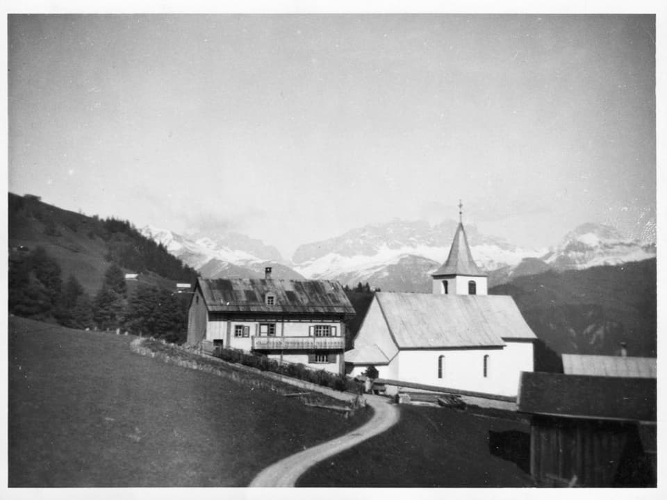 Schwarzweiss-Fotografie einer Kirche. Gleichdaneben ein Pfarrhaus.