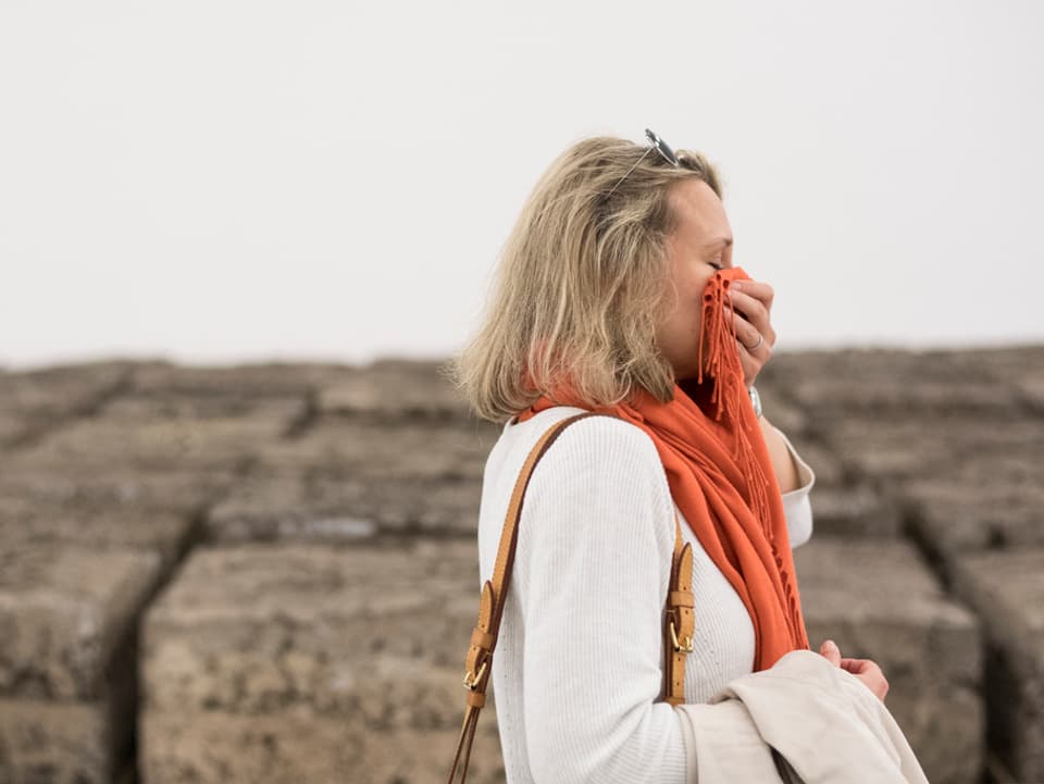 Eine Frau steht vor den Fäkalkunst-Blöcken und hält sich mit dem Schal die Nase zu
