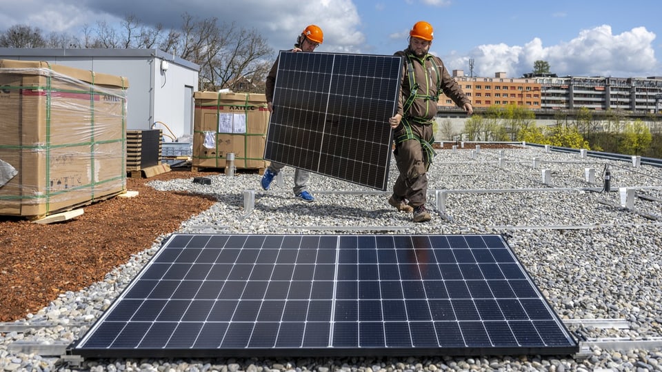Zwei Männer installieren Fotovoltaik-Anlage auf einem Dach.