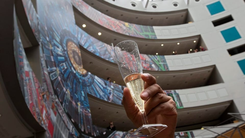 Eine Person hält ein Champagnerglas in die Höhe im Cern-Foyer.