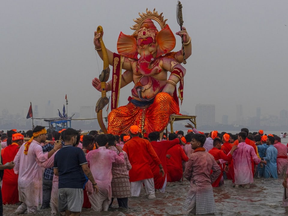 Die Statue des elefantenköpfigen Hindu-Gottes Ganesha im Wasser. Rundherum stehen Gläubige in nassen Kleidern.