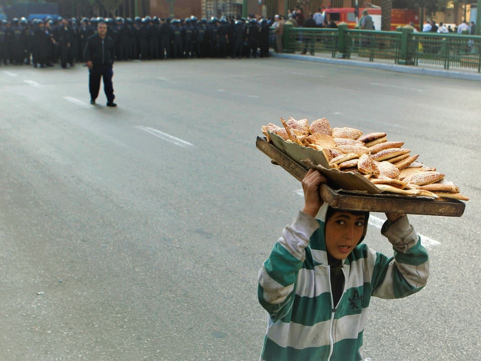 Ein Junge, der Brot auf dem Kopf trägt, rennt während regierungsfeindlicher Proteste in der Innenstadt von Kairo vor einer Kolonne von Bereitschaftspolizisten weg.