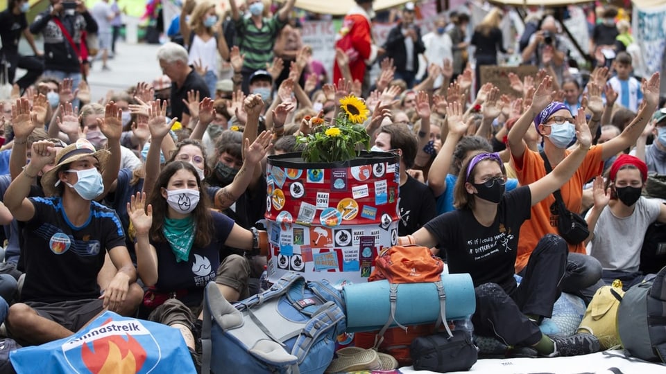 Klimaaktivisten sitzen auf dem Bundesplatz, sie tragen Fahnen und Coronamasken über dem Gesicht.