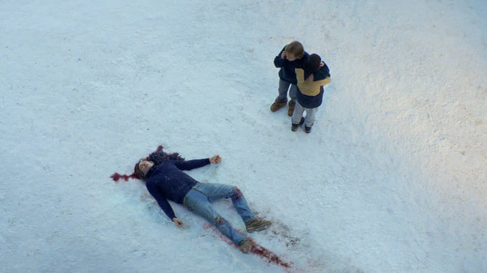 Mann liegt reglos im Schnee, Blut um den Kopf. Daneben stehen zwei Personen, Foto von oben auf Köpfe runter.
