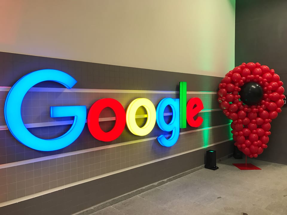Das Google-Logo vor einer grauen Wand im Treppenhaus.