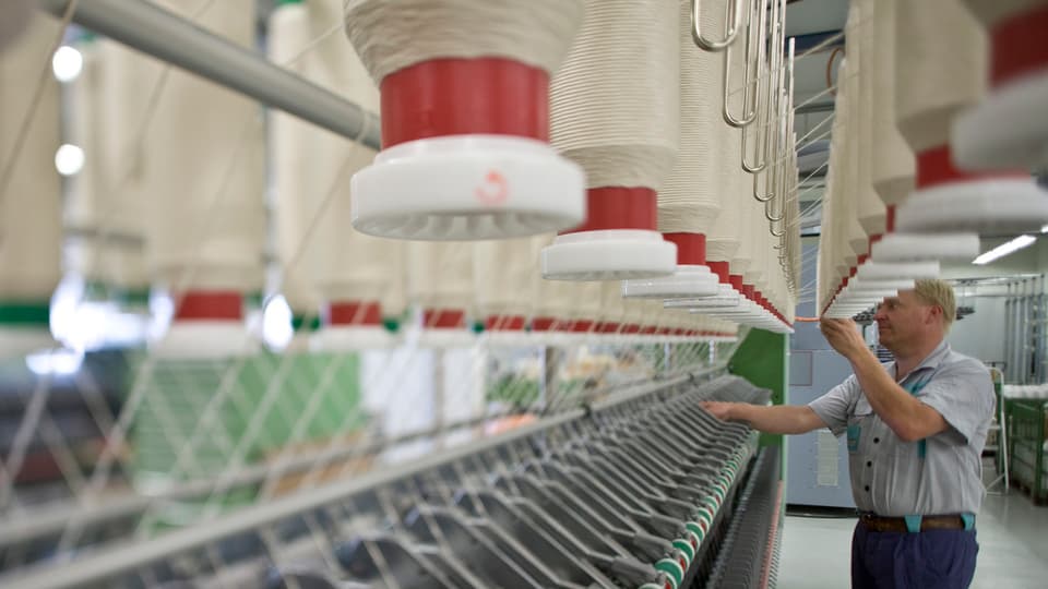 Ein Arbeiter von Rieter in Winterthur kontrolliert die Spindeln an einer Textilmaschine.