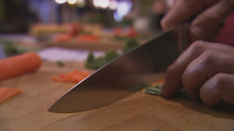 Mann schneidet Petersilie mit einem Kochmesser.
