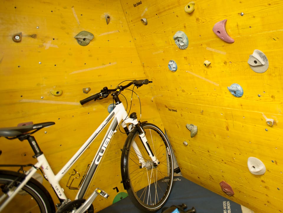 Ein weisses Fahrrad steht vor einer gelben Kletterwand.