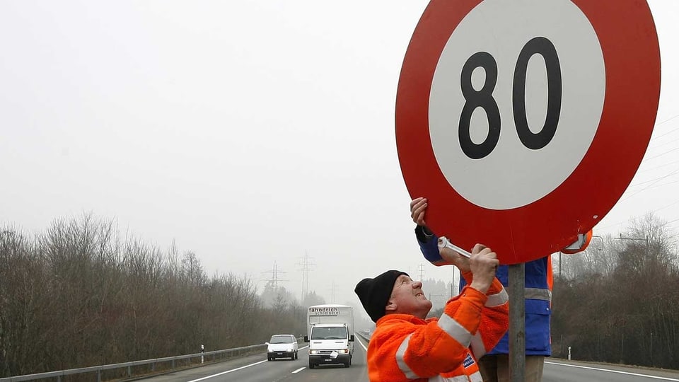 Arbeiter montieren auf einer Autobahn ein Tempo-80-Schild. (keystone)