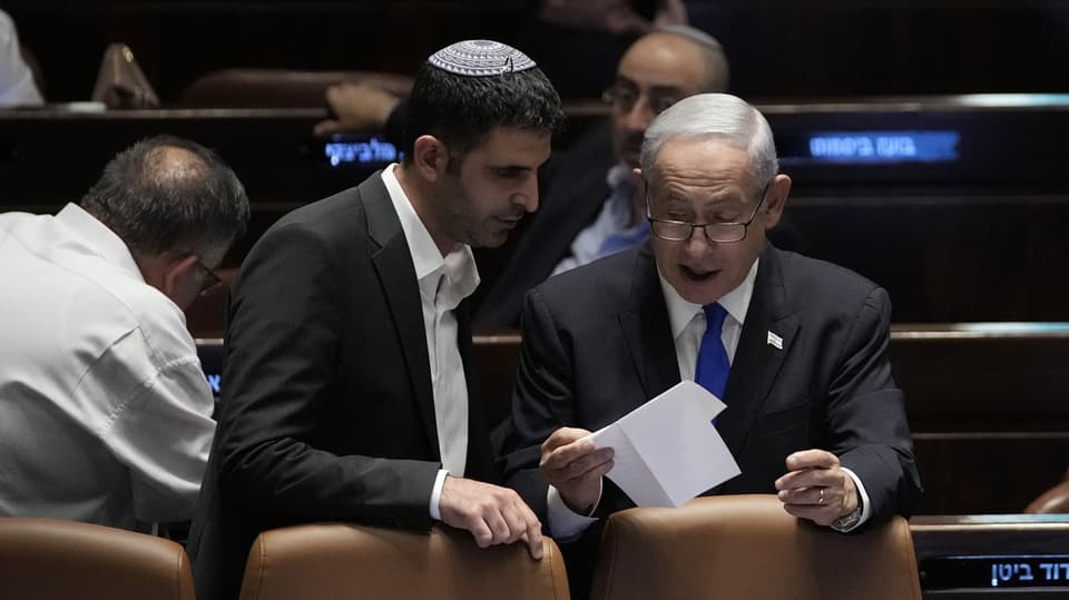 Benjamin Netanjahu steht rechts neben einem Mann. Netanjahu hält ein Stück Papier in der Hand.