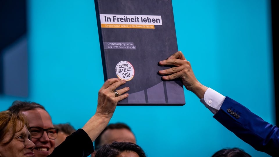 Hände halten ein Buch mit dem Titel «In Freiheit» leben' bei einer Veranstaltung hoch.