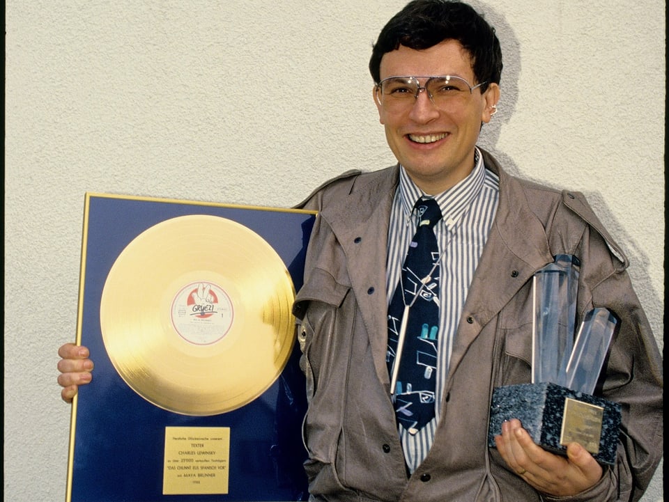 Ein Mann in brauner Jacke mit Golderener Schallplatte und einem weiteren Preis in den Armen.