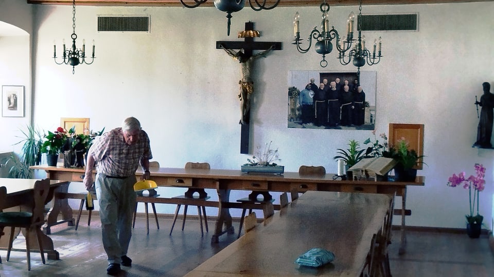 Älterer Mann geht durch eine Raum mit langen Tischen und Kronleuchtern