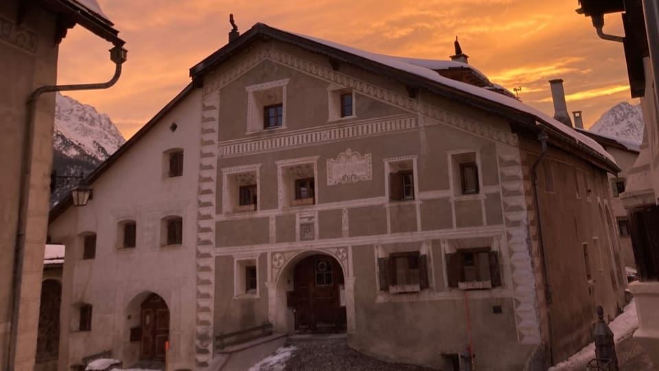 Grosses Haus vor rötlichem Sonnenuntergangs-Himmel. Grau angestrichen mit weissen Verzierungen.