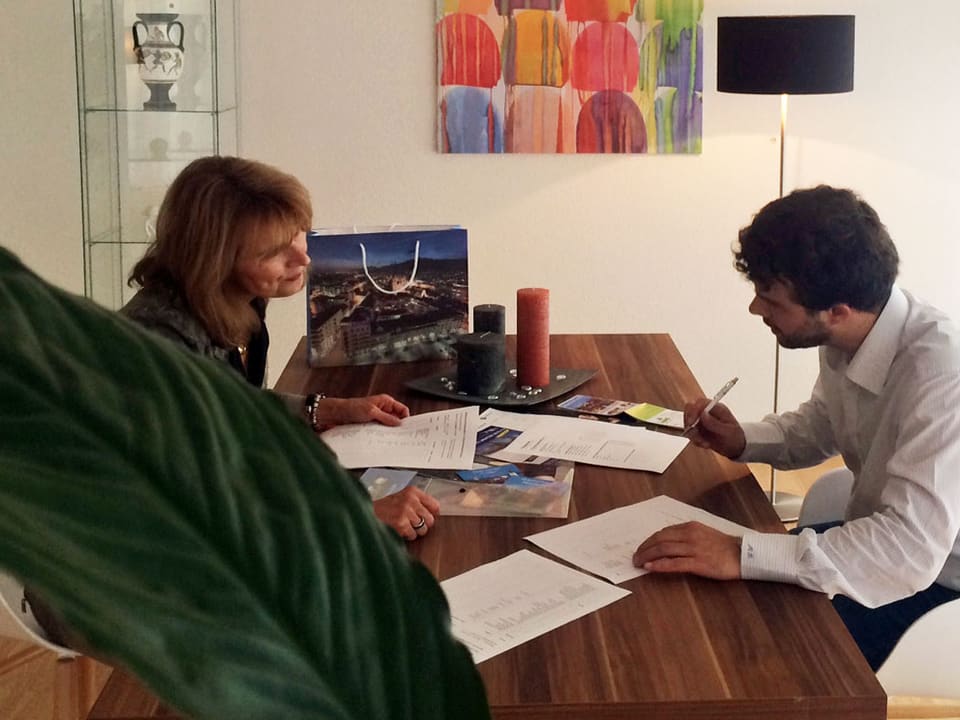 Büchler trägt ein weisses Hemd, Dreitagebart und dunkle Haare. Er unterzeichnet ein Dokument am Tisch. Gegenüber sitzt Susanne Blaser vom Oltener Projektteam.