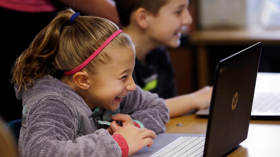Mädchen in der Schule am Laptop, lacht sich weg