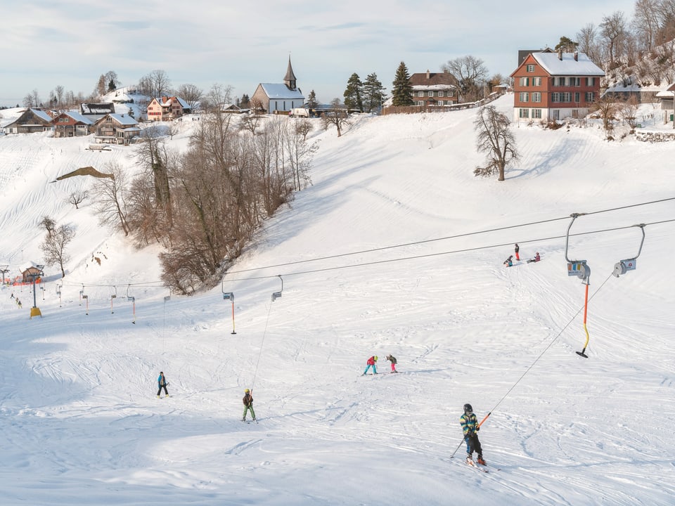 Blick auf Sternenberg im Schnee. Auf dem Skilift fahren mehrere Kinder.