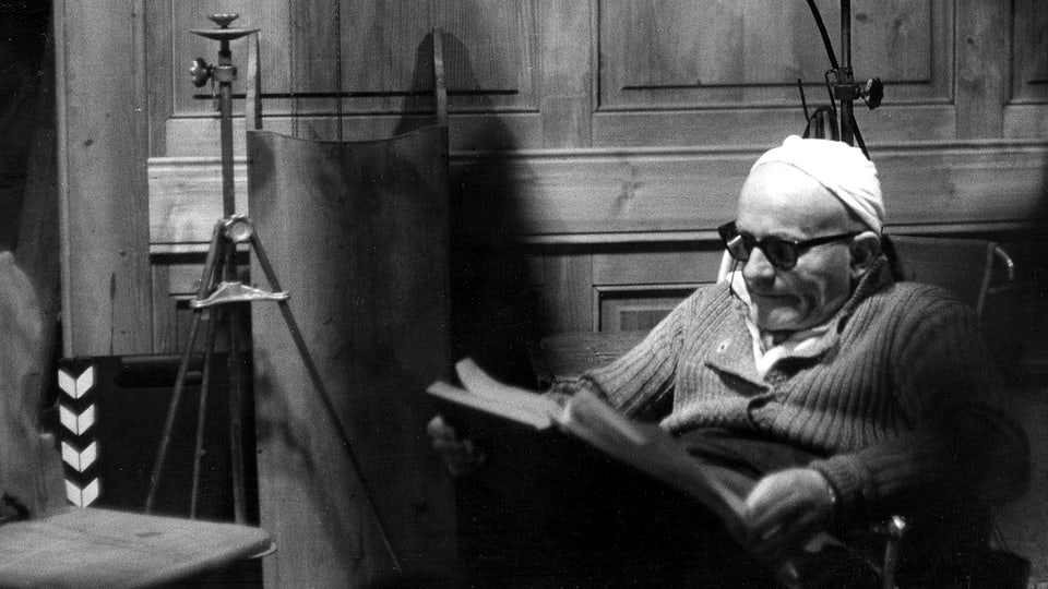 Ein älterer Mann sitzt auf einem Regiestuhl und liest im Drehbuch.