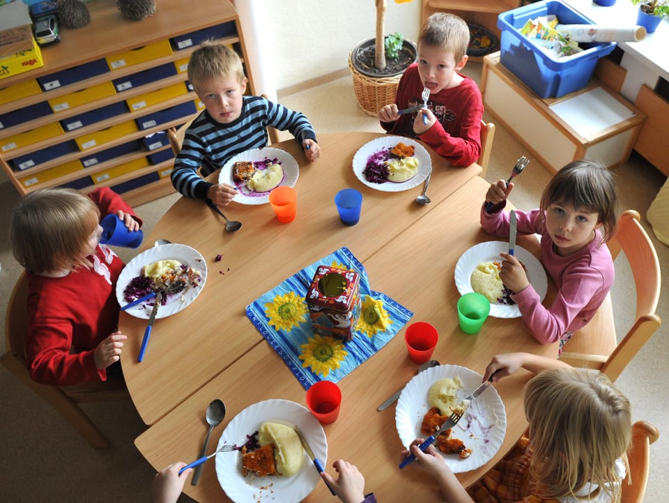 Kinder sitzen an einem runden Tisch und essen.